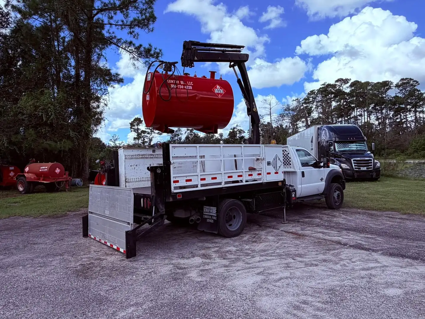 Flatbed truck with a crane lifting a red Gentry Oil skid fuel tank into place